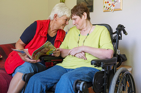 Eine Patientin im Rollstuhl mit ihrer Pflegerin