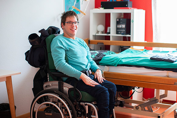 Ein Mann im Rollstuhl zeigt stolz sein Zimmer