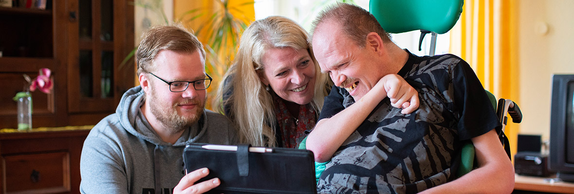 Ein Nutzer der SWG Grohn schaut mit zwei Mitarbeitern auf ein Tablet-PC