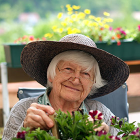 Eine ältere Dame mit Strohhut sitzt an einem Blumenkasten